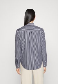 Navy and white striped shirt with long sleeves, button cuffs, and a pointed collar. Features a curved hem and a back yoke.