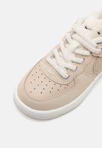 Ljust beige läder sneakers med perforerat tåbox, fleecefodrad tunga, vita snören och gummisula med strukturerade mönster.