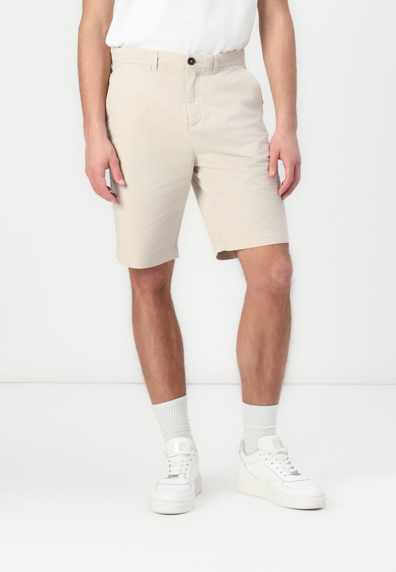 Beige katoenen shorts met een getailleerde fit, knoopsluiting en zijzakken, gecombineerd met witte sneakers en geribbelde crew-sokken.