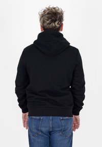 Sudadera con capucha negra hecha de una tela suave, que cuenta con un bolsillo tipo canguro y puños de canalé, combinada con unos jeans de mezclilla azul.