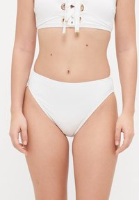 White bikini top with lace-up detail and gold accents, paired with high-waisted white bikini bottoms. Smooth, stretchy fabric.