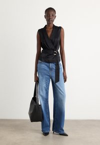 Black wrap top with a belt, blue wide-leg jeans, and black pointed heels; accessorized with a black tote bag; smooth textures.