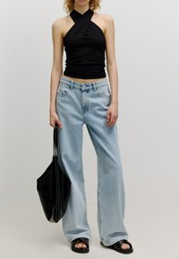 Zwarte haltertop, lichtblauwe wijde jeans, zwarte tote bag en zwarte slidesandalen. Soepele stoffen; relaxte pasvorm; casual stijl.