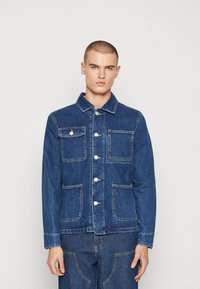 Giacca di jeans blu con colletto, chiusura anteriore con bottoni e quattro tasche. Il design presenta cuciture in evidenza e una superficie liscia.