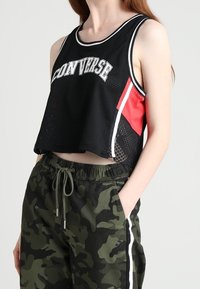 Svart mesh-crop top med vita detaljer och texten "CONVERSE"; matchas med kamouflagebyxor med sidosträck och elastisk midja.