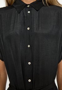 Mustriline collariga must särk, valmistatud kergest struktureeritud kangast, millel on pärliliste nööpidega ja lühikesed varrukad.