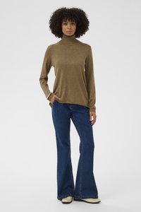 Brauner Rollkragenpullover aus weichem Strick, kombiniert mit ausgestellten blauen Denim-Jeans und hellen Schuhen. Einfaches Design mit geripptem Hals.