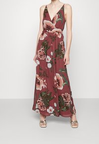 Blommig maxiklänning med djup V-ringning, med en vinröd bakgrund och rosa och gröna blommönster, samt en knytning vid midjan.