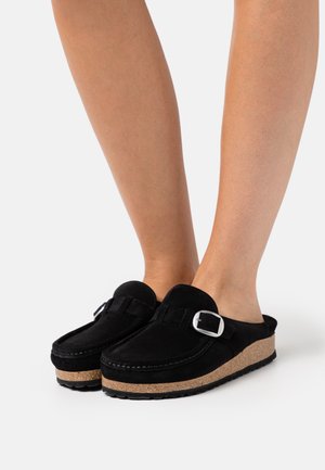 Black suede clogs with a cork sole, featuring a silver buckle accent and a slip-on design. Smooth texture with a rounded toe.
