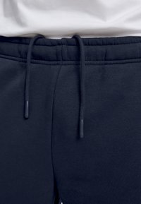 Navy blue sweatpants, joissa on joustava vyötärö, varustettuna narulla muovipäillä ja sileällä pinnalla.