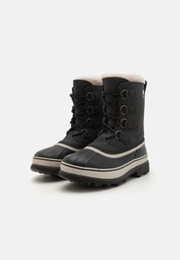 Zwarte winterlaarzen met een getextureerde rubberen zool, vetersluiting, nepbontvoering en een contrasterende grijze streep langs de zool.