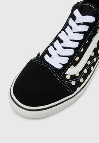 Mustad suedesneakerite valgete paeltega, mille pealmine osa on valmistatud pehmest kangast, kaunistatud väikeste kollaste ja valgete lillemustriga. Valge kummitald.