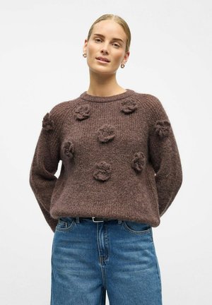 Ruda megzta megzta suknelė su tekstūriniais gėlių raštais priekyje, apvaliu iškirpimu ir laisvu siluetu, derinama su mėlynomis džinsinėmis kelnėmis.