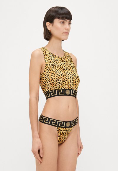 Dzeltenais leopardu raksta bikini komplekts, kas sastāv no bez piedurknēm topa ar melnu Grieķu atslēgas rakstu un atbilstošām zemu uzliktām biksēm.