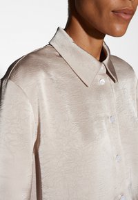 Camicia button-up beige, strutturata, con un sottile motivo increspato e colletto classico. Presenta bottoni bianchi e una vestibilità rilassata.