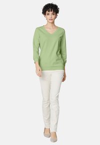 Lichtgroene V-hals trui met driekwartmouwen, gecombineerd met witte slim-fit broek en beige schoenen, op een neutrale achtergrond.