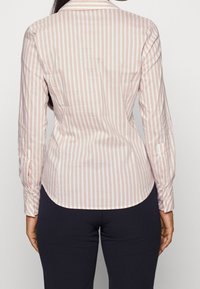 Camicia a righe rosa chiaro e bianca realizzata in tessuto morbido, con colletto classico, maniche lunghe con polsini bottonati e orlo curvo.