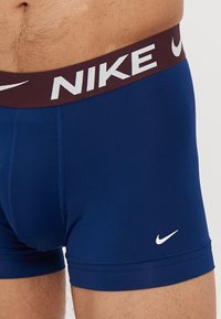 Mornarčasto plave biciklističke kratke hlače sa širokim bordo pojasom na kojem je bijeli natpis "NIKE" i mali bijeli logo na donjem prednjem dijelu.