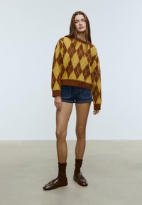 Brun og gul argyle strikket sweater, cropped design, lange ærmer. Kombineret med mørke denim shorts og brune snørebåndsko med sokker.