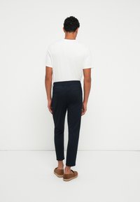 Pantaloni navy sartoriali con gambe affusolate, vita elastica e due tasche posteriori, abbinati a una maglietta bianca a girocollo e sandali marroni.