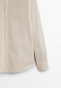 Chemise à motif vichy beige et crème avec manches longues, fermeture par boutons et ourlet arrondi. Tissu doux avec une texture lisse.