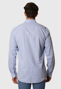 Camisa de manga larga azul claro hecha de tejido texturizado, con puños abotonados, rayas sutiles y un dobladillo curvado en la parte trasera.