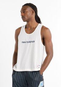 White mesh tank top with a loose fit, featuring "new balance" embroidered in navy blue. Paired with black and blue striped shorts.