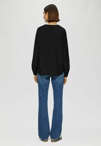 Zwarte longsleeve top met een ronde halslijn, gecombineerd met blauwe flare denim jeans, gezien van achteren, met een relaxte pasvorm.
