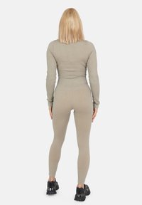 Geribbelde olijfgroene twee-delige set bestaande uit een nauwsluitend langmouwtop en legging, gecombineerd met zwarte chunky sneakers.