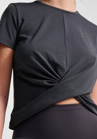 Mörkgrå atletisk topp i lätt tyg, med en vriden framsida och korta ärmar. Slät textur med minimal märkning.