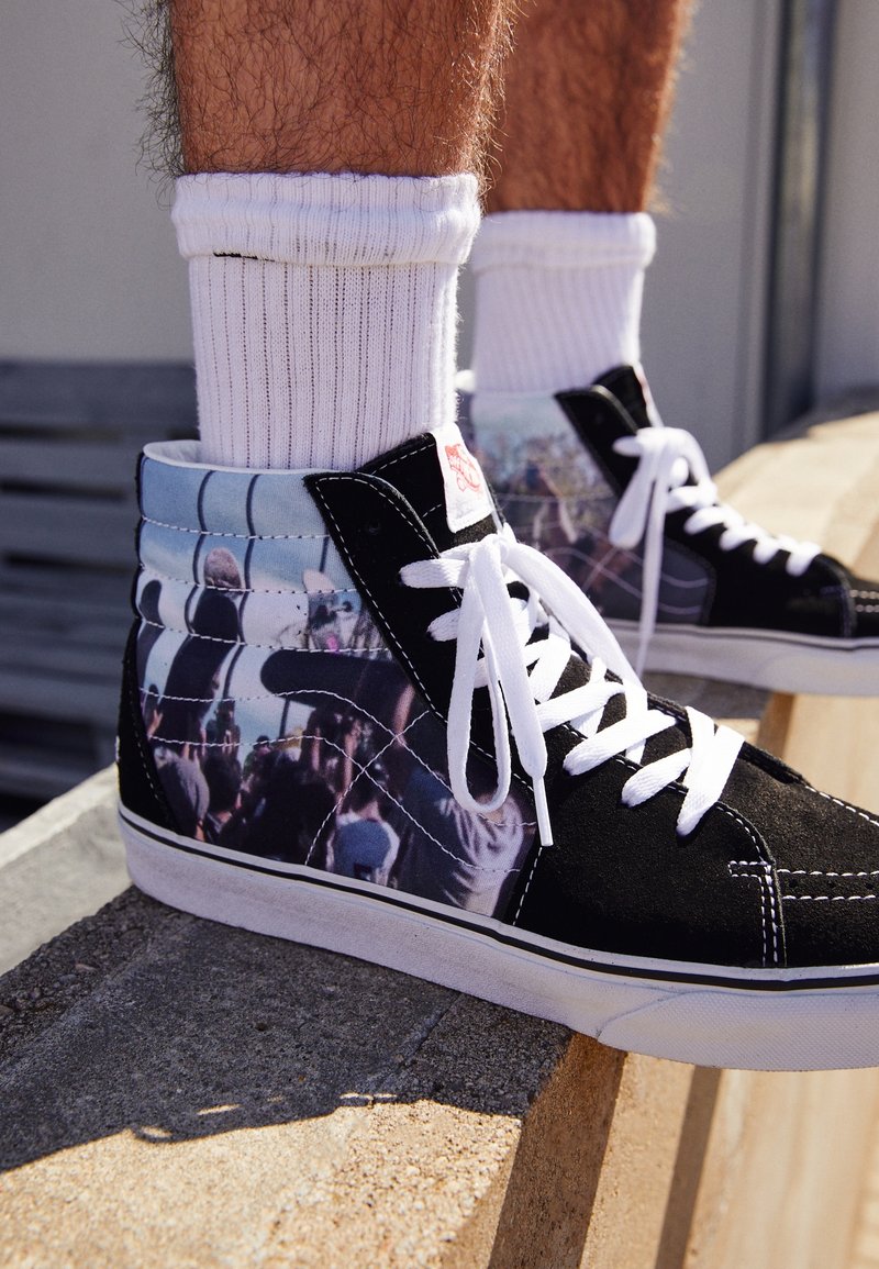 Sorte high-top sneakers med et fotografisk mønster på siderne, hvide snørebånd og gummisål. Har kontrasterende sort suedemateriale og canvasmateriale.