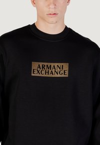 Sudadera negra de algodón con un logotipo rectangular de rayas doradas "ARMANI EXCHANGE" centrado en el pecho. Diseño clásico de cuello redondo.