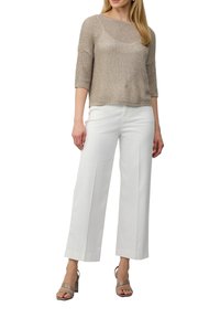 Beige gestrickter Pullover mit Dreiviertelärmel, kombiniert mit weißen weit geschnittenen Hosen. Das Model trägt hellgraue Blockabsatzsandalen.