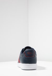 Marinblå lädersneakers med röda accenter, vit gummisula, texturerad baksida och logotypdetalj n ära klacken. Låg design med vadderad krage.