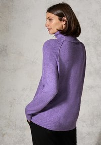 Lila gestrickter Pullover mit hohem Kragen, seitlichen Taschen und gerippten Bündchen. Weicher Stoff und lockere Passform.