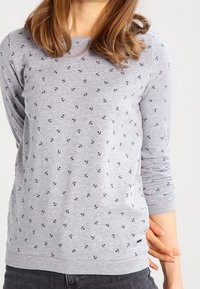 Sudadera gris con pequeño patrón de anclas en azul marino, cuello redondo y mangas largas. Presenta puños y dobladillo acanalados para un ajuste ceñido.