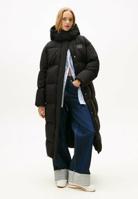 Zwarte pufferjas met een hoge kraag, met een sluiting aan de voorkant met knopen. Gekocht met een wijde blauwe jeans en witte sneakers.