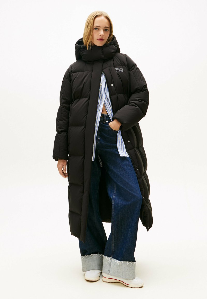 Zwarte pufferjas met een hoge kraag, met een sluiting aan de voorkant met knopen. Gekocht met een wijde blauwe jeans en witte sneakers.
