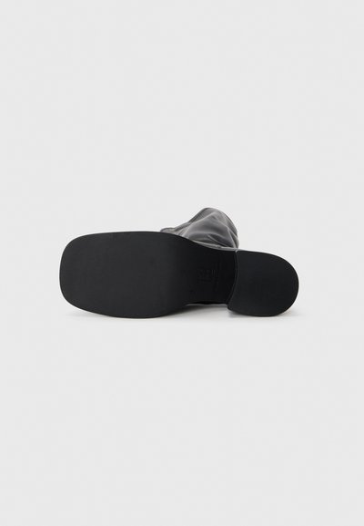 Black ankle boot with a smooth leather upper, flat rubber sole, and rounded toe, featuring a subtle seam detail along the sides.