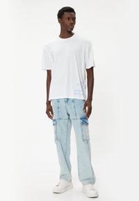 Vit kortärmad t-shirt med ljusblå text. Kombinerad med ljusblå baggy denimjeans med fickor och vita sneakers.