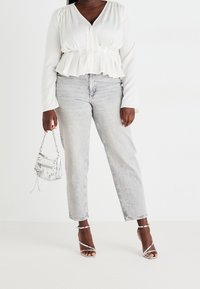 Blusa blanca de manga larga tipo peplum, jeans de tiro alto y pierna recta en gris claro, tacones plateados con tiras y un pequeño bolso de mano plateado.