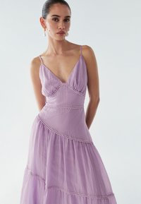 Lavendelfarbenes, fließendes Maxikleid mit verstellbaren Spaghettiträgern, V-Ausschnitt und gestuften, strukturierten Lagen. Abgeschlossen mit dekorativen Nähten.