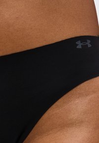 Κοντινό πλάνο του γοφού ενός ατόμου που φοράει μαύρα αθλητικά εσώρουχα Under Armour με εμφανές λογότυπο στη μέση.