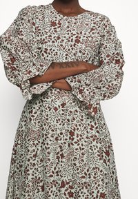 Blommönstrad klänning i ljus mintgrön med vinröda blommor, med långa volangärmar och rund halsringning. Mjuk tygg med intrikata mönster.