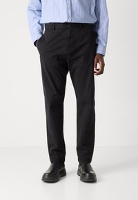 Black cotton trousers with a relaxed fit, featuring a front button closure and side pockets, paired with black boots and a blue striped shirt.