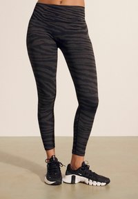 Svarta leggings med ett strukturerat grått zebramönster, hög midja, i kombination med svarta sportskor med vita sulor.