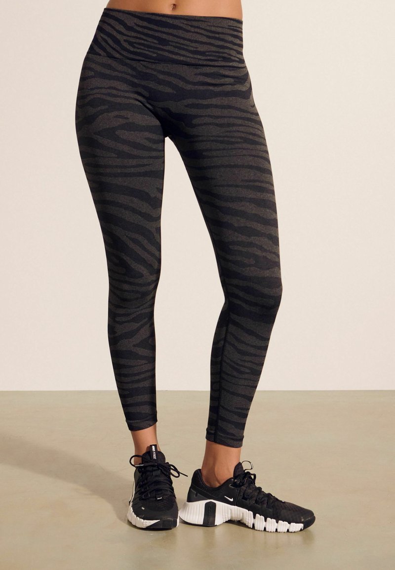 Svarta leggings med ett strukturerat grått zebramönster, hög midja, i kombination med svarta sportskor med vita sulor.