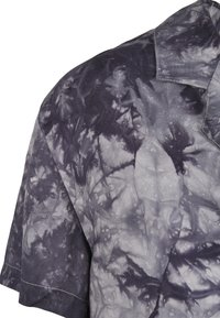 Koszula z krótkim rękawem w ciemnoszarym kolorze z wzorem tie-dye; ma wyrazisty kołnierzyk i widoczne szwy wzdłuż krawędzi.