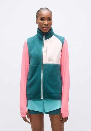 Fleecevest in teal met lange roze mouwen, een rits aan de voorkant en een klein borstzakje. Voorzien van gestructureerde stof en een logopatch.