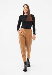 Black long-sleeve top, tan pleated trousers, and black knee-high boots. Smooth fabric with tailored fit, side pockets, and sleek design.